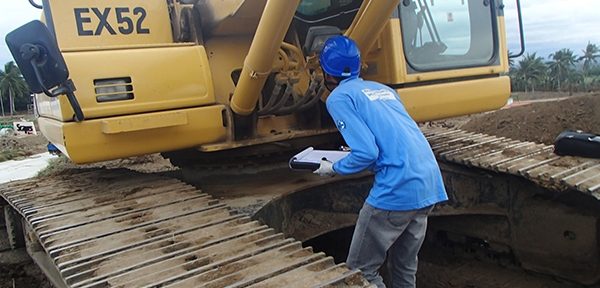 An inspector recording findings on a clipboard beside a tracked excavator on site