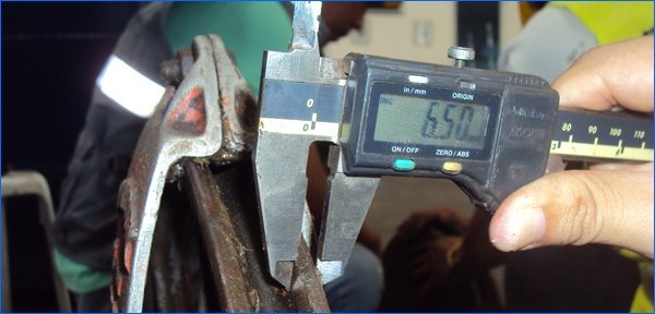 A digital caliper measuring the throat opening of a crane hook during an inspection